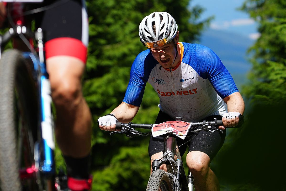 Ein Mountainbiker fährt mit schmerzverzerrtem Gesicht einen Anstieg hinauf. 