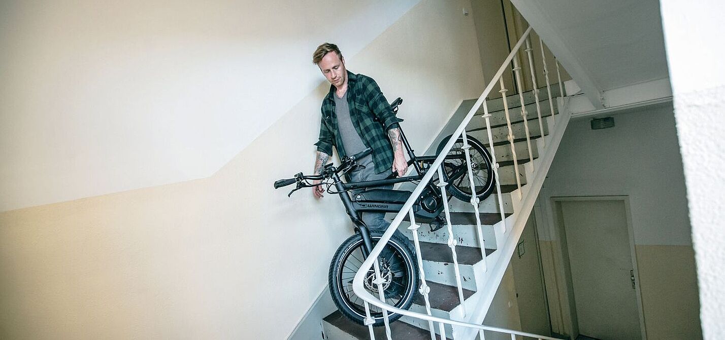 Fahrrad im Treppenhaus Ein Mann trägt ein Fahrrad in einem Treppenhaus.