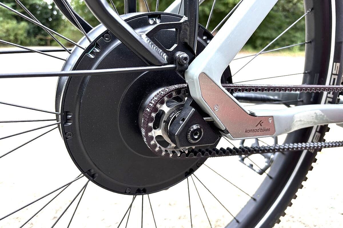 Großaufnahme eines schwarzen Hinterradmotors, davor der Antriebsrimen, an einem grauen Fahrrad. 