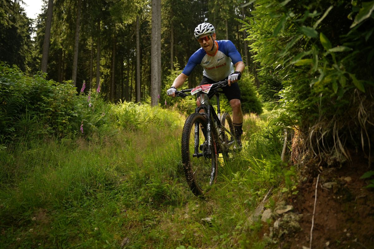 Ein Mountainbiker fährt auf einer grasbewachsenen Strecke im Wald bergab. 